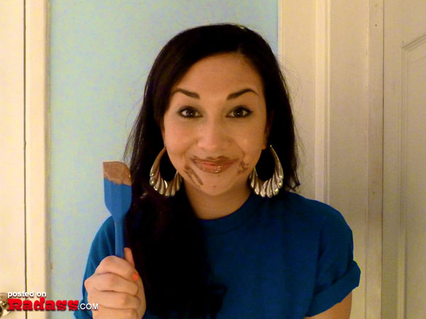 A woman in a blue shirt holding a blue spatula, expressing 