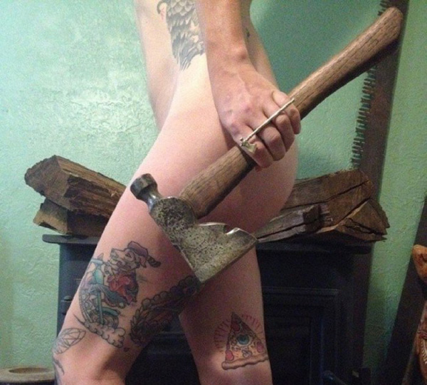 A woman with tattoos holding an axe in front of a fireplace, emitting an aura that says 