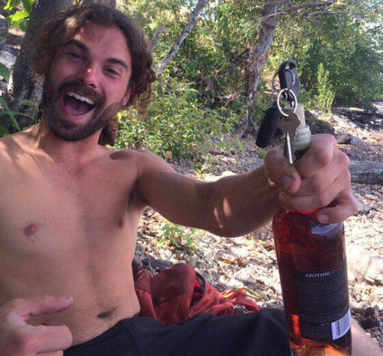 A man, shirtless but confidently holding a bottle of wine, defying conventions with his unconventional yet effective choice.