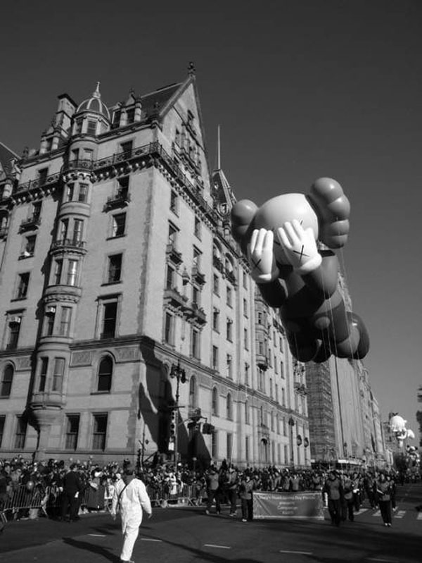 A black and white photo of a balloon flying over a city during Macy's Day Parade.