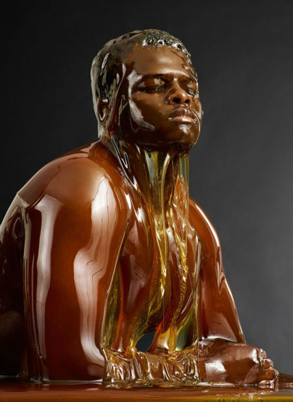 A sculpture featuring a black man seated, drenched in honey.