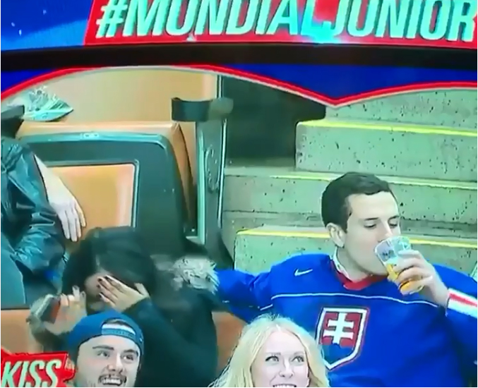 A group of people awkwardly sitting in a stadium watching a hockey game on the Kiss Cam.
