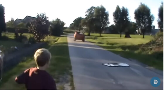 A boy walking down a road with a car behind him in the "Shut Up And Take My Money (Video)".