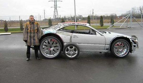 A man standing next to a WTF silver car with a tire on it.