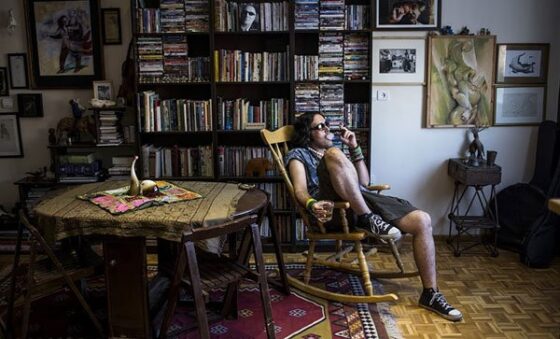 A man sitting in a rocking chair in a room with bookshelves and a table, offering Another View On Iran.