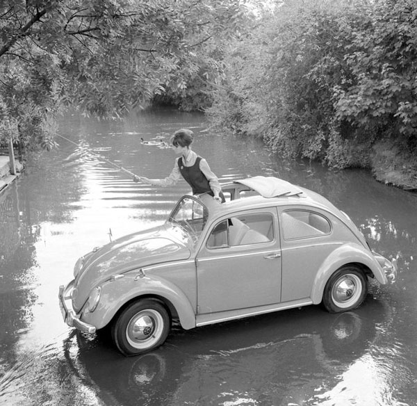 A woman perched on a Volkswagen Beetle submerged in water.