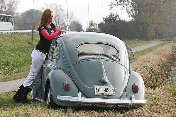 A babe is leaning against the side of a VW Beetle.