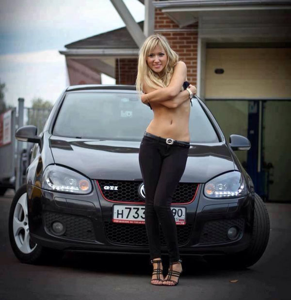 A blond babe posing next to a black Volkswagen Golf.