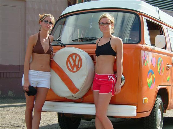 Two babes posing with a nostalgic VW bus.
