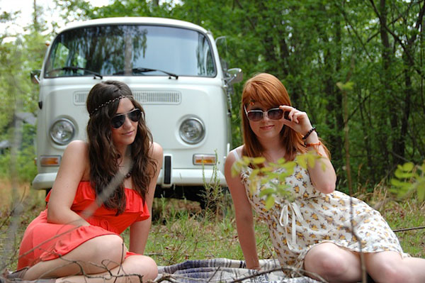 Two babes lounging on a blanket next to a colorful VW bus.