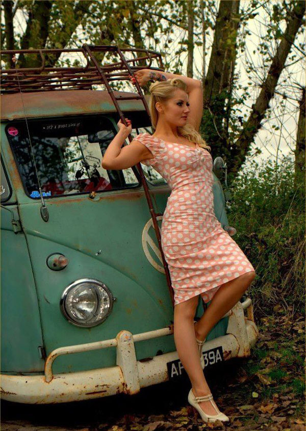 A babe in a dress leaning against a VW bus.