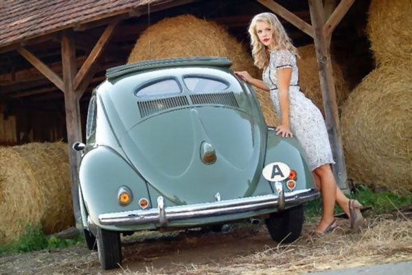 A babe is posing next to a green Volkswagen Beetle.