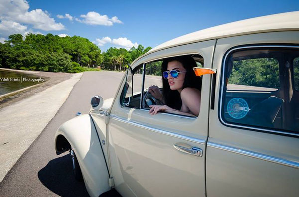 A babe is cruising in a VW Beetle donning sunglasses.