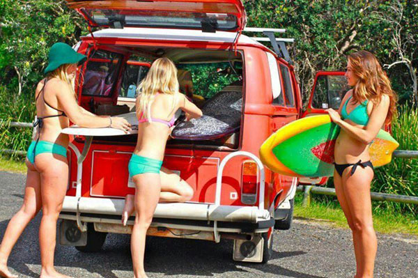 Three babes in bikinis next to a van with surfboards.