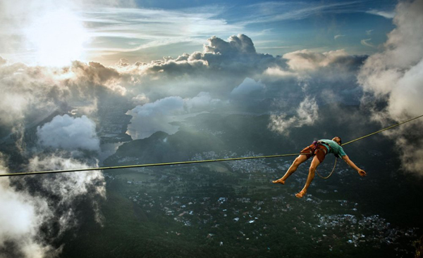 A man is performing the art of balance on a rope in the mesmerizing heights above the clouds, captured in one of the 50 cool ass photos.
