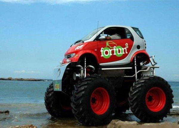 A cool smart car with large tires navigating the sand.