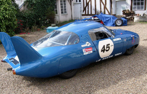 A blue race car is parked in front of a house. (Keywords: Cool Ass Cars)