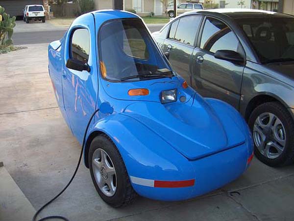 A cool blue electric car parked in front of a car.