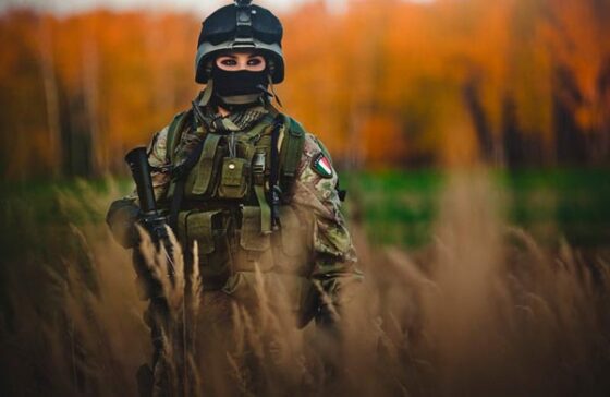 A soldier is standing in a field with a rifle, exuding strength and intensity.