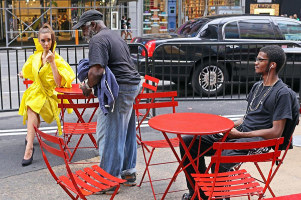 In New York City, a man in a yellow raincoat sits at a red folding table, captured in one of the 49 awesome photos of daily life.