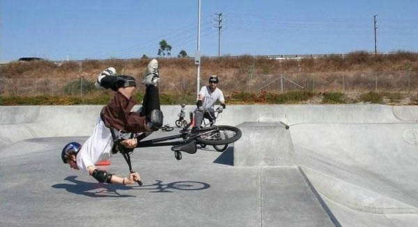 A man doing a trick on his bike at a skate park, unfortunately face plants.