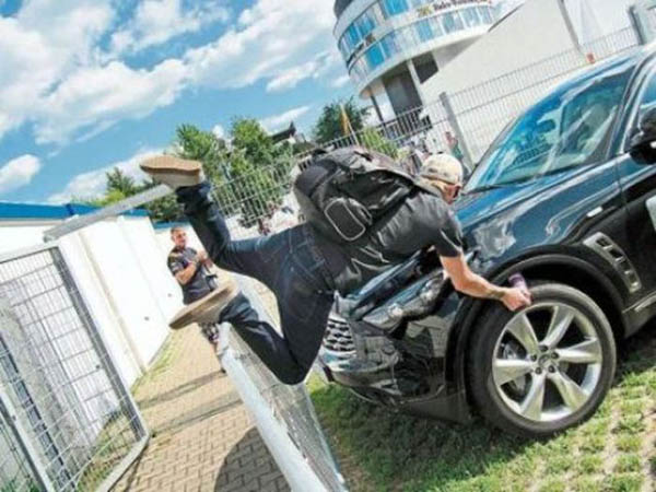 A man face plants while jumping on top of a car in front of a fence.