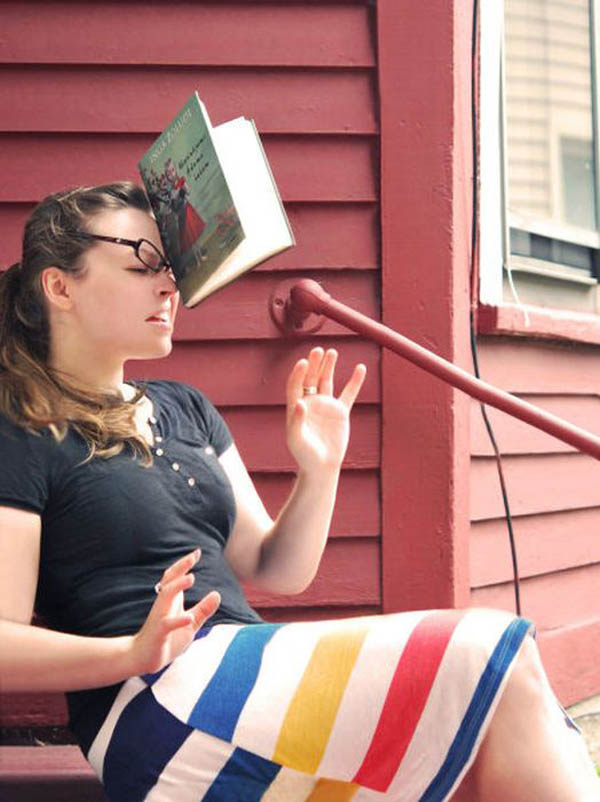 A woman face plants while sitting on a porch with a book on her head.