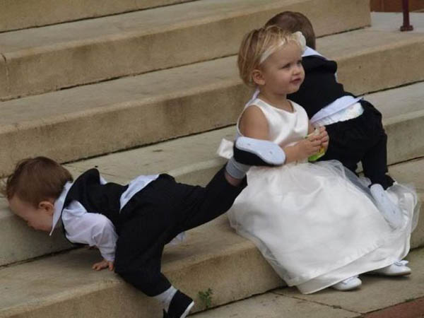 A little girl in a dress and tuxedo is playing on the steps, occasionally face planting.
