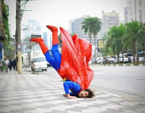 A man in a superman costume doing a handstand on the street, face plants.