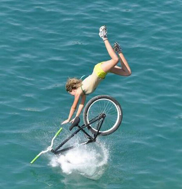 A woman face plants while doing tricks on a bike in the water.