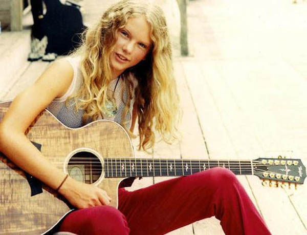 A young woman, one of the famous artists before making the big time, sitting on a wooden deck with an acoustic guitar.