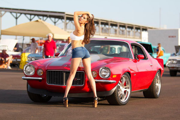 A woman striking a pose beside the perfect combination of a red muscle car.