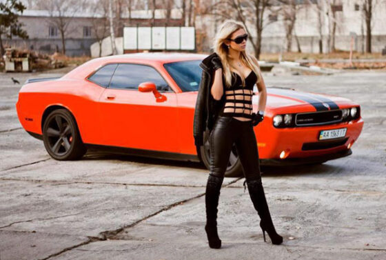 A woman in black leather standing next to the perfect combination of an orange Dodge Challenger.