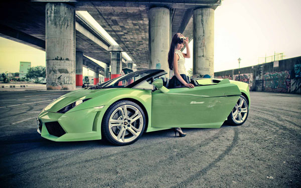 A woman is striking a pose in front of the perfect combination of a green sports car.