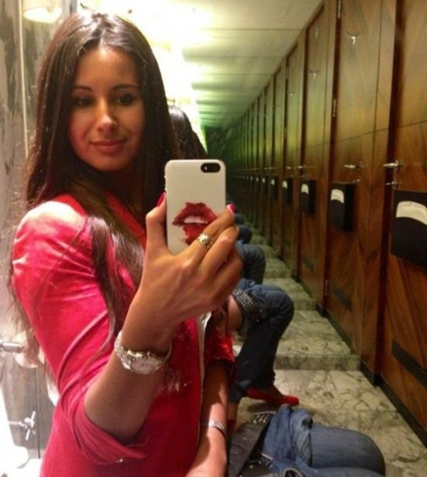 A woman is taking a selfie in a bathroom, but she can't help but notice one flaw.