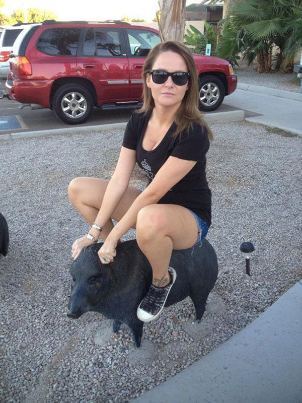A woman playfully perched on a statue of a pig.