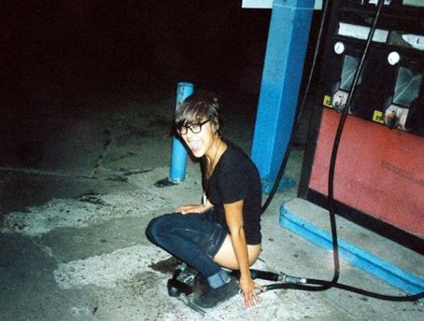 A woman kneeling down next to a gas pump, sporting an 