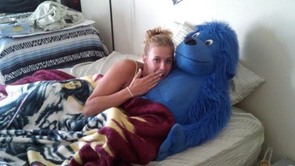 A woman cuddling with a blue stuffed animal in bed.