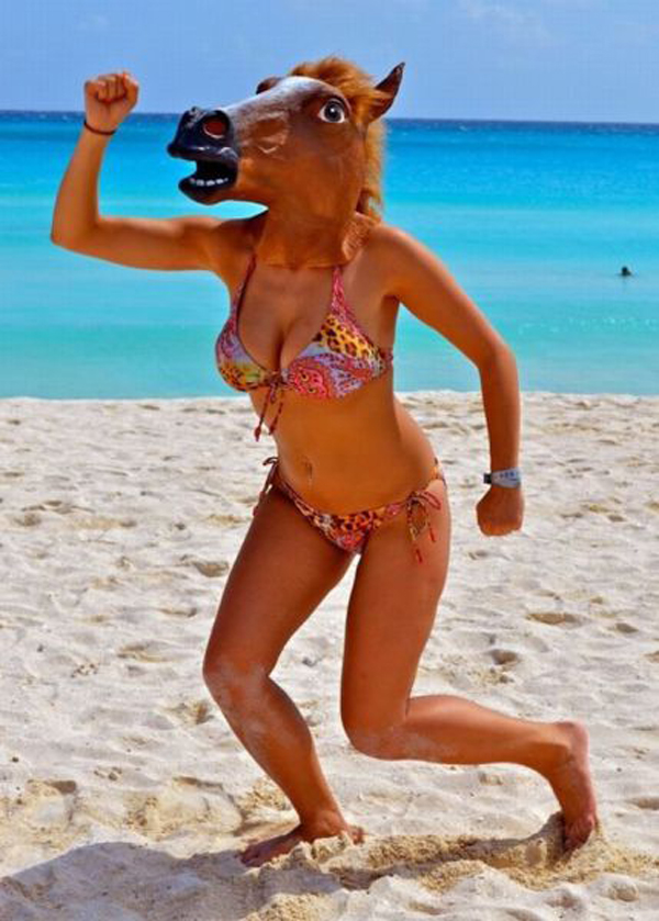 A woman in a bikini wearing a *horse mask* on the beach.