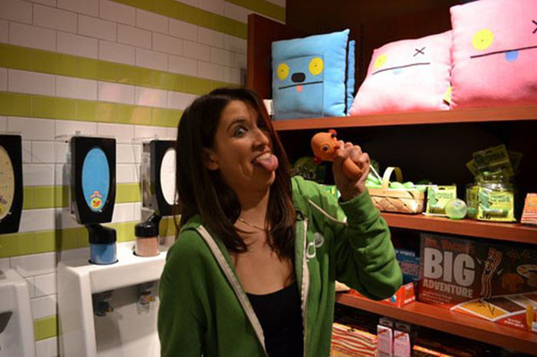A woman in a green hoodie eating a toy in a bathroom, displaying quirks that would make one say 