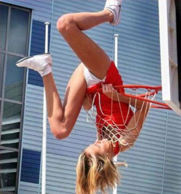 A skilled girl performing a daring stunt on a basketball hoop.
