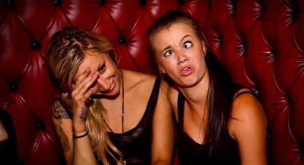 Two women sitting in a red booth with their faces covered, contemplating 