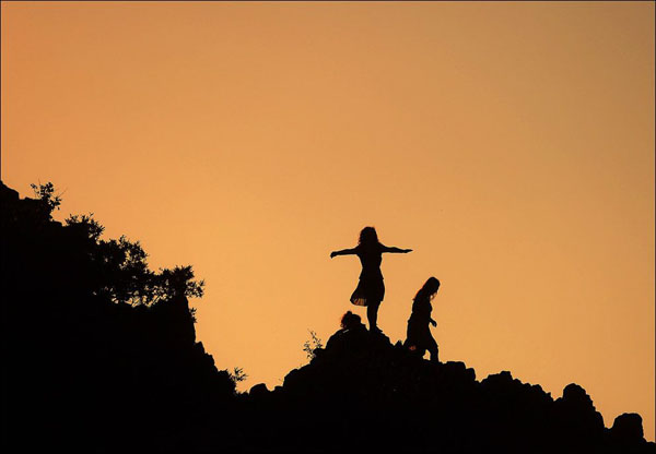 Two people standing in silhouette on a majestic mountain peak.