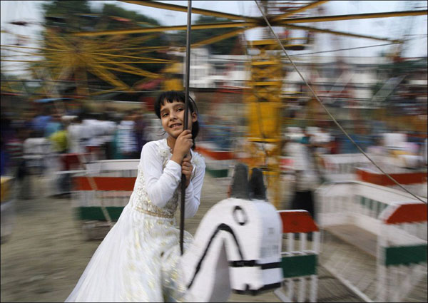 A girl in a white dress enjoys a carousel ride at an amusement park, capturing the beauty of the world.