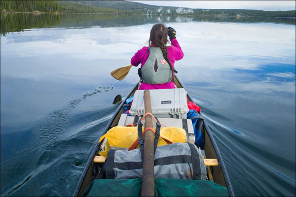 A woman paddling a canoe in a beautiful lake.
