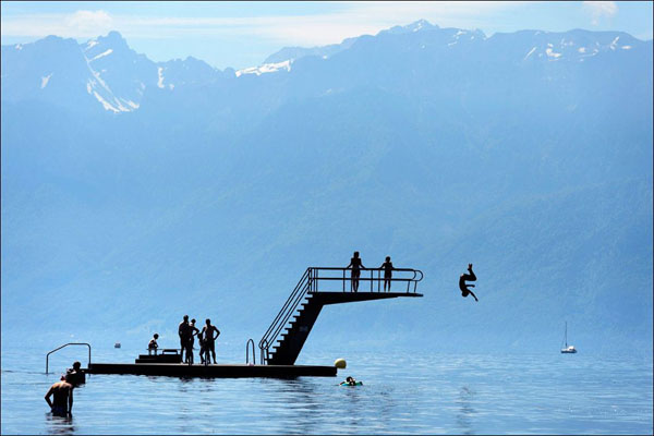 A group of people jumping into a lake, showcasing the beautiful world with mountains in the background.