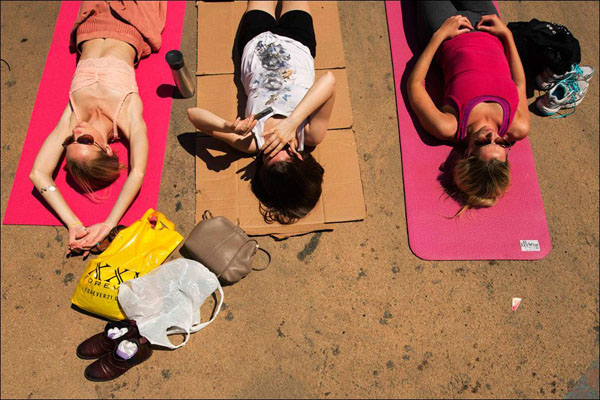 Three beautiful women practicing yoga on mats outdoors in the city.