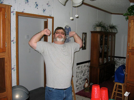 A man flexing his muscles in a living room, showcasing his Bro-like traits.