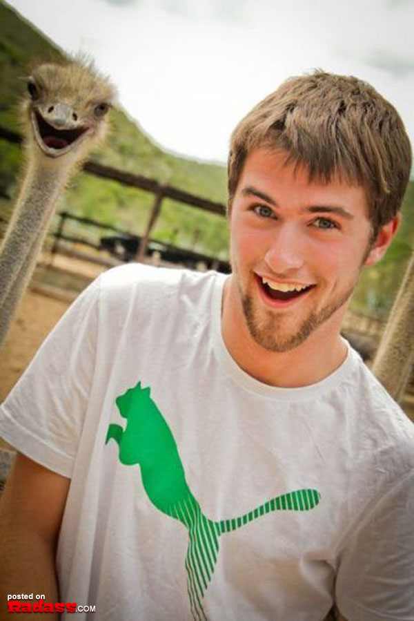 A young man skillfully photobombs an ostrich with a smile.