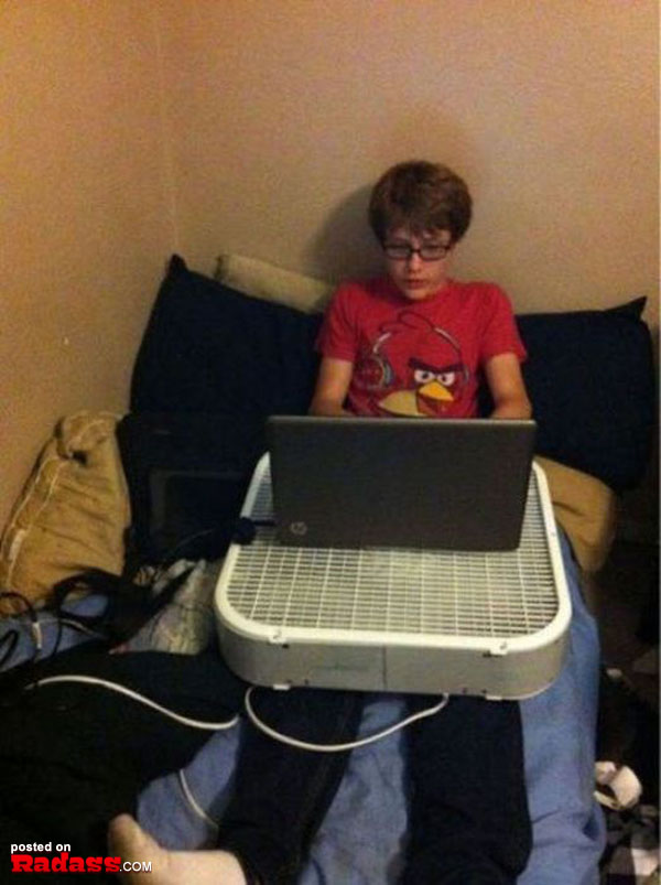 A young man using his laptop on a bed while referencing 